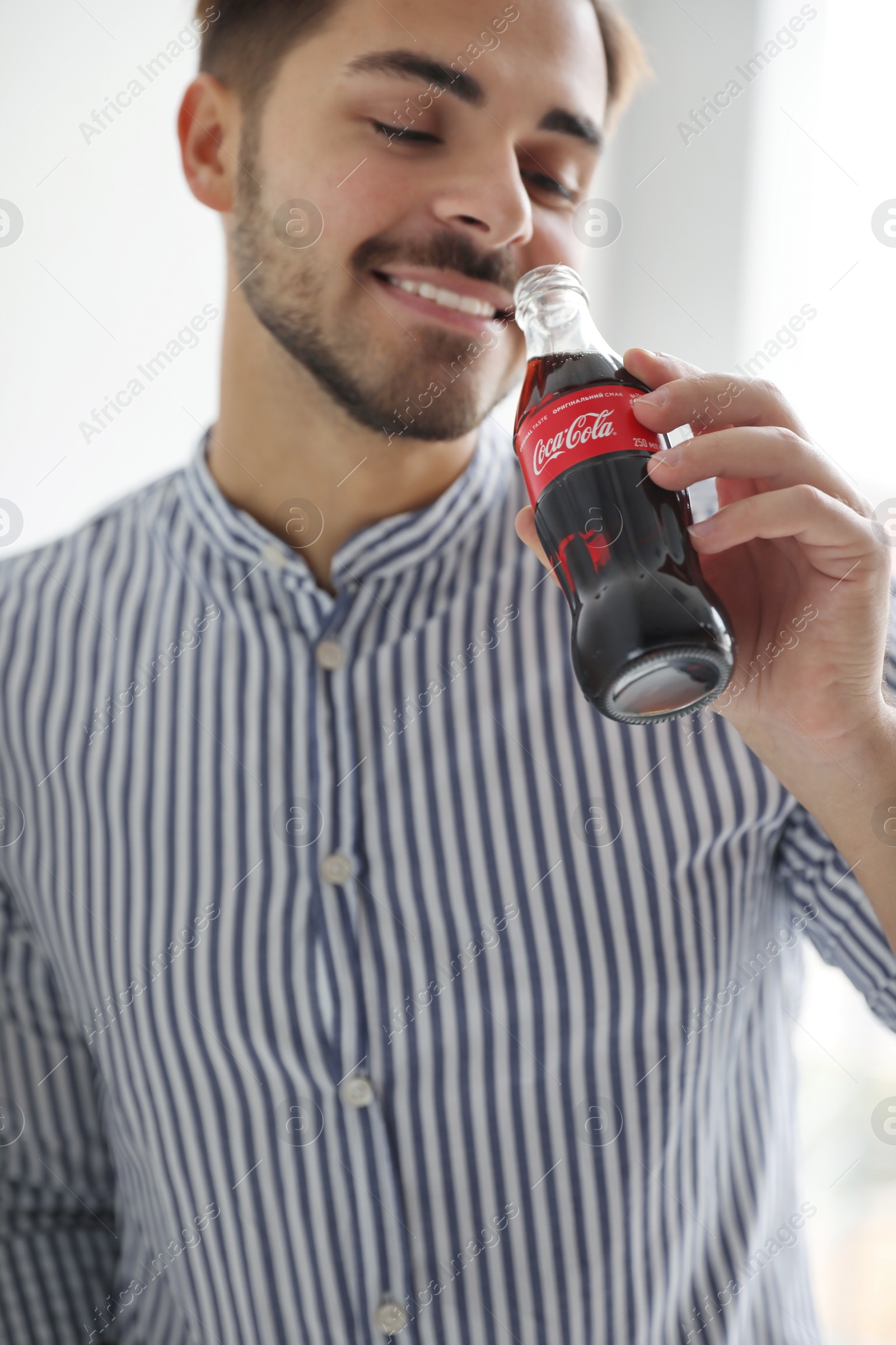 Photo of MYKOLAIV, UKRAINE - NOVEMBER 28, 2018: Young man with bottle of Coca-Cola indoors