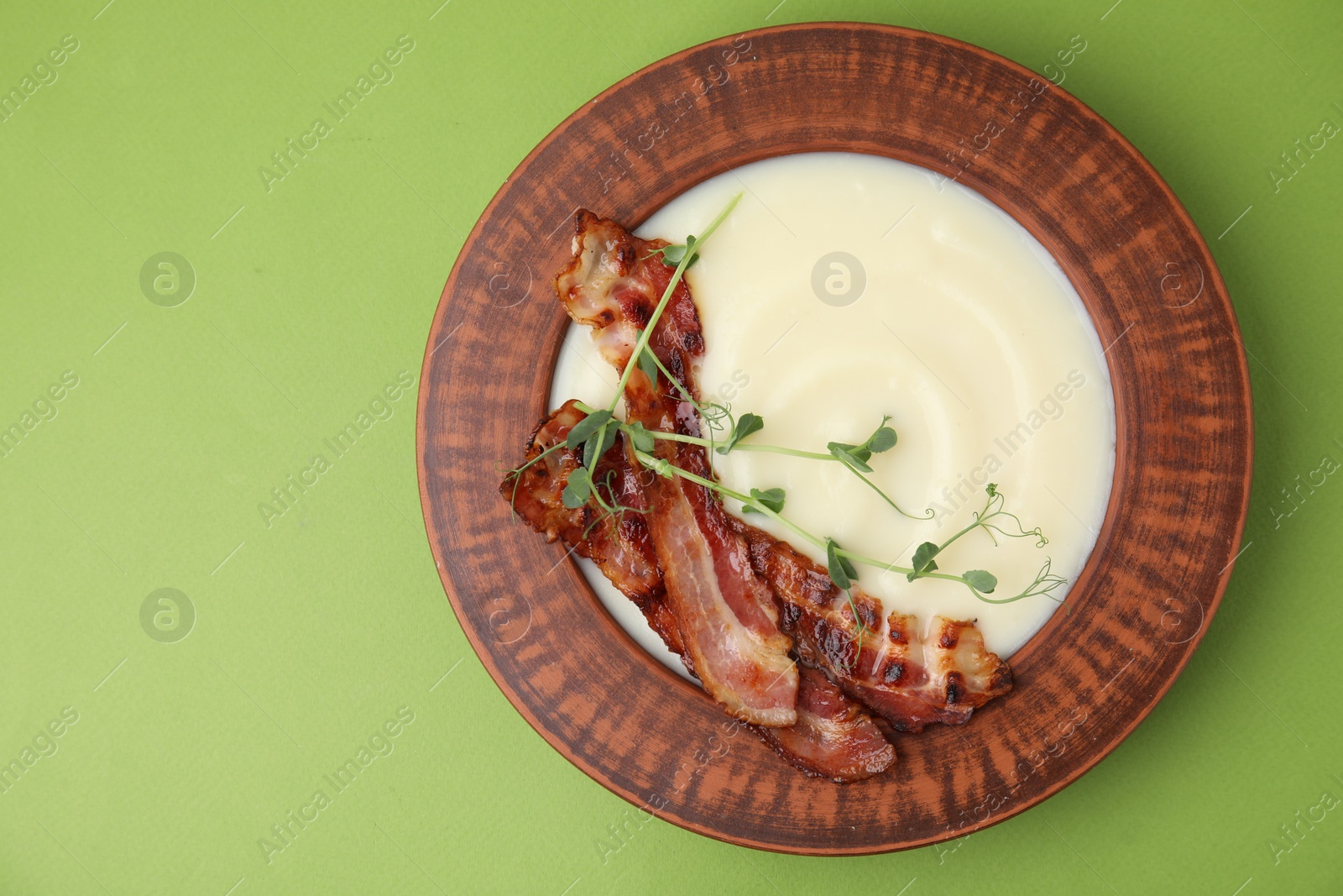 Photo of Delicious potato soup with bacon and microgreens in bowl on green table, top view. Space for text