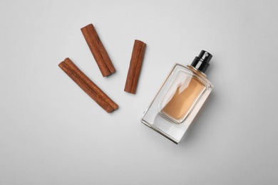 Photo of Bottle of perfume and cinnamon sticks on light background, top view