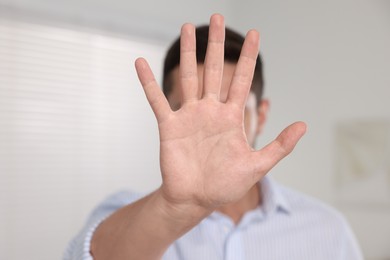 Photo of Man showing stop gesture indoors, selective focus