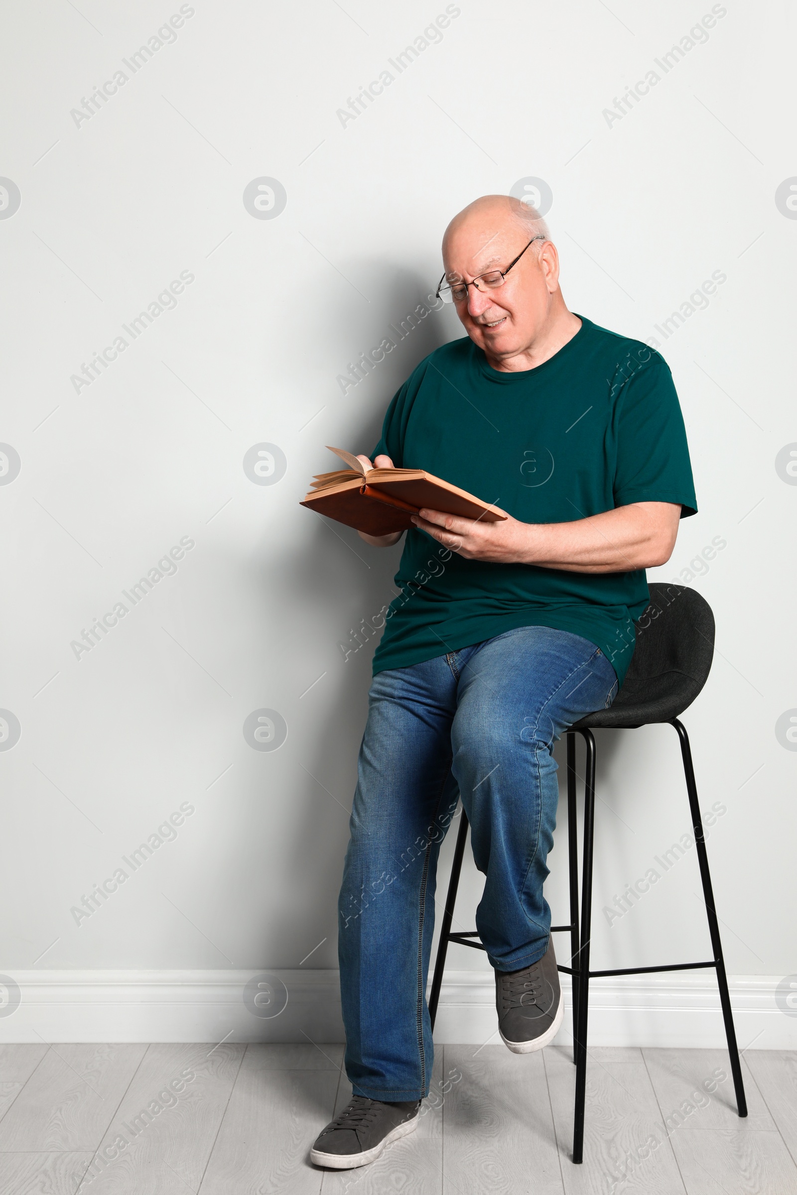 Photo of Portrait of senior man with glasses reading book near light wall