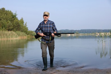 Photo of Man with hunting rifle near lake outdoors