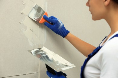 Photo of Professional worker plastering wall with putty knives, closeup