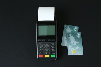 Photo of New modern payment terminal and credit cards on black background, flat lay