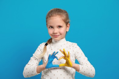 Little girl making heart with her hands painted in Ukrainian flag colors on light blue background. Love Ukraine concept