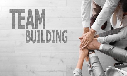 Image of People holding hands together over light wooden background, top view. Team building