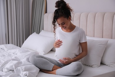 Pregnant young African-American woman sitting on bed at home