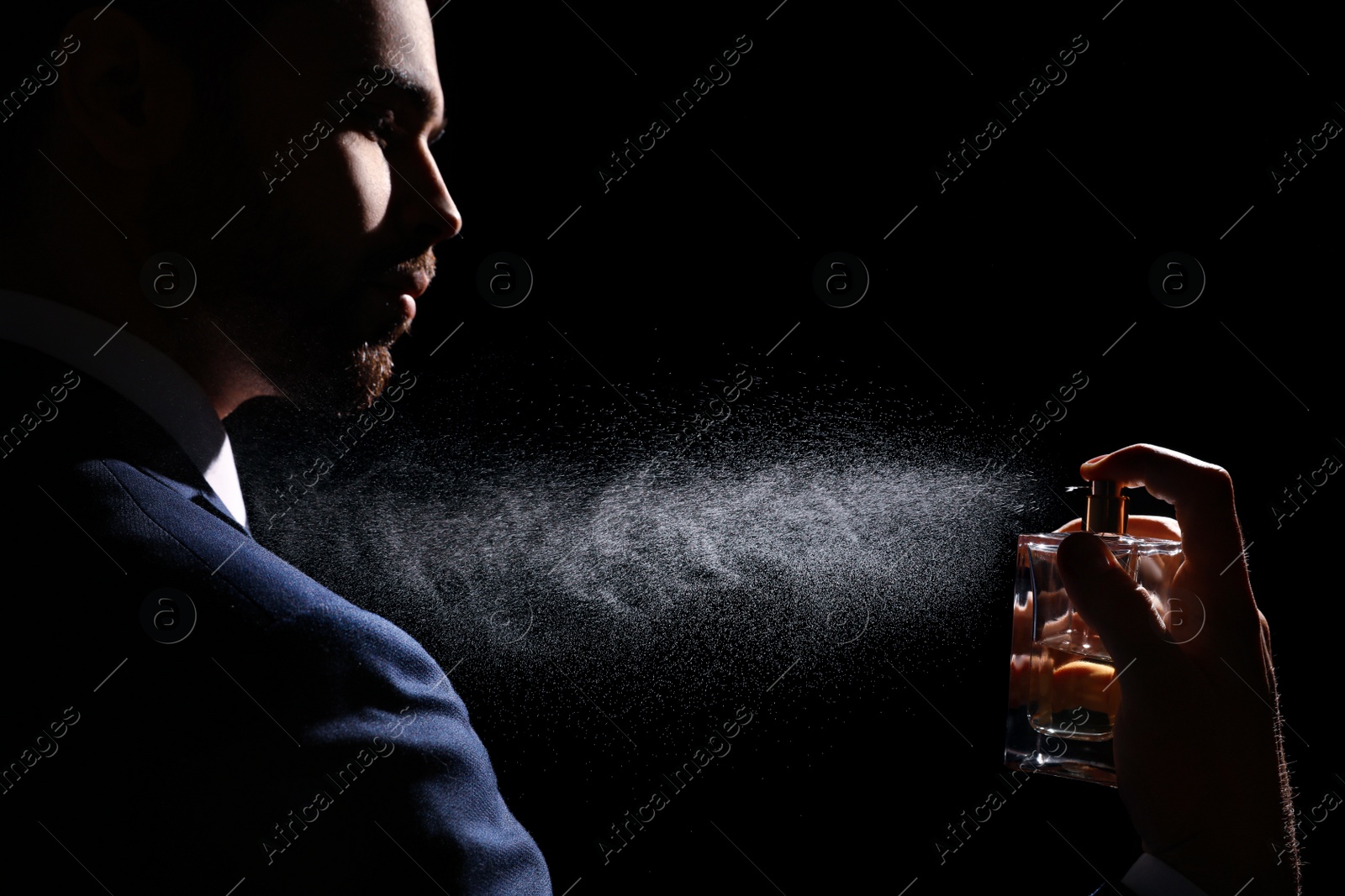 Photo of Man spraying luxury perfume on black background, closeup