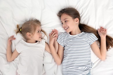 Photo of Cute little sisters on bed, top view