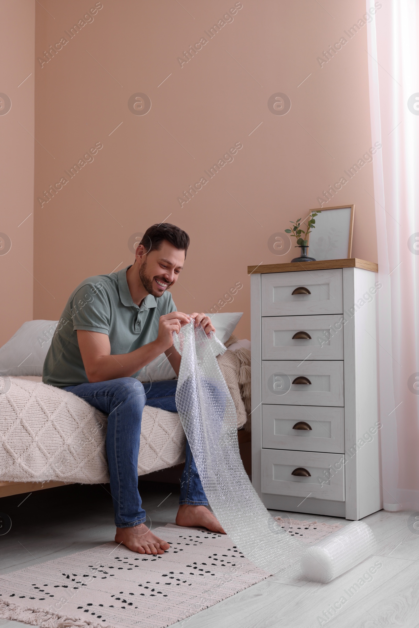 Photo of Man popping bubble wrap in bedroom at home. Stress relief