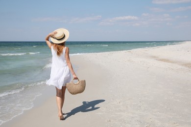Photo of Woman with beach bag and straw hat near sea, back view