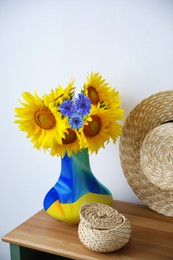 Image of Bouquet of beautiful flowers, wicker box and hat on wooden table indoors