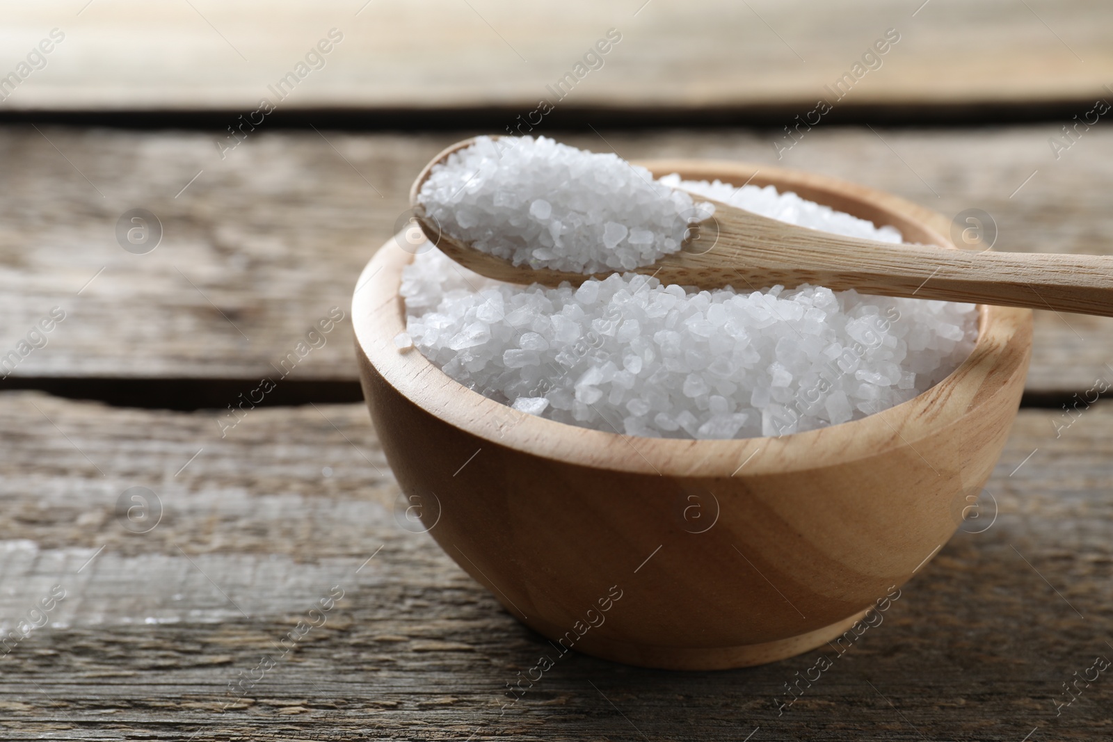 Photo of Organic salt in bowl and spoon on wooden table, closeup. Space for text