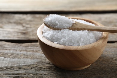 Photo of Organic salt in bowl and spoon on wooden table, closeup. Space for text