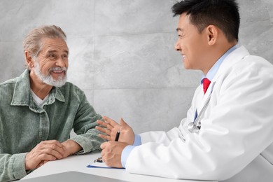 Doctor consulting senior patient at white table in clinic