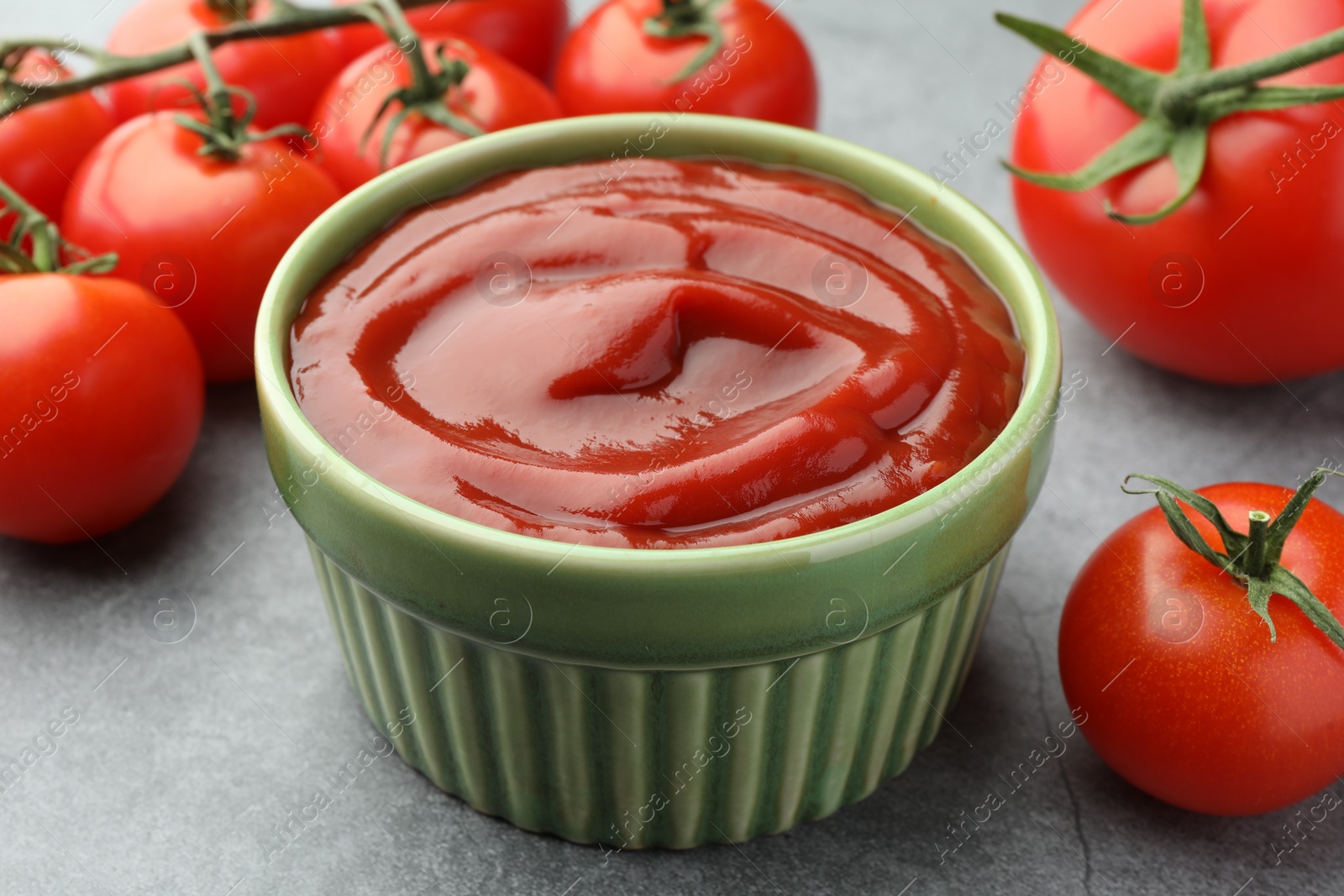 Photo of Bowl of tasty ketchup and tomatoes on light grey table, closeup