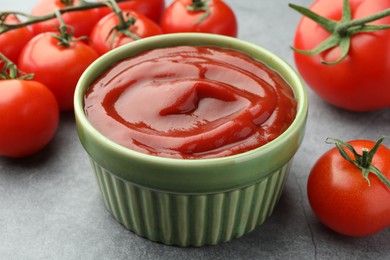 Bowl of tasty ketchup and tomatoes on light grey table, closeup