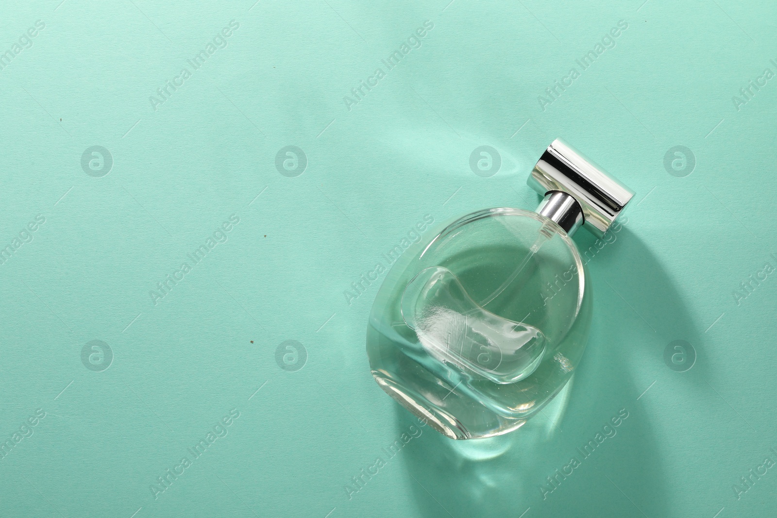 Photo of Luxury perfume in bottle on turquoise background, top view. Space for text