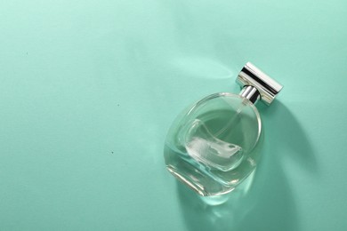 Photo of Luxury perfume in bottle on turquoise background, top view. Space for text