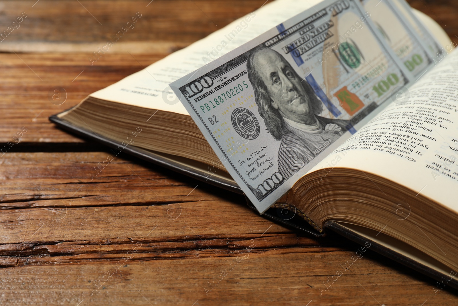 Photo of Open Bible with money on wooden table, closeup