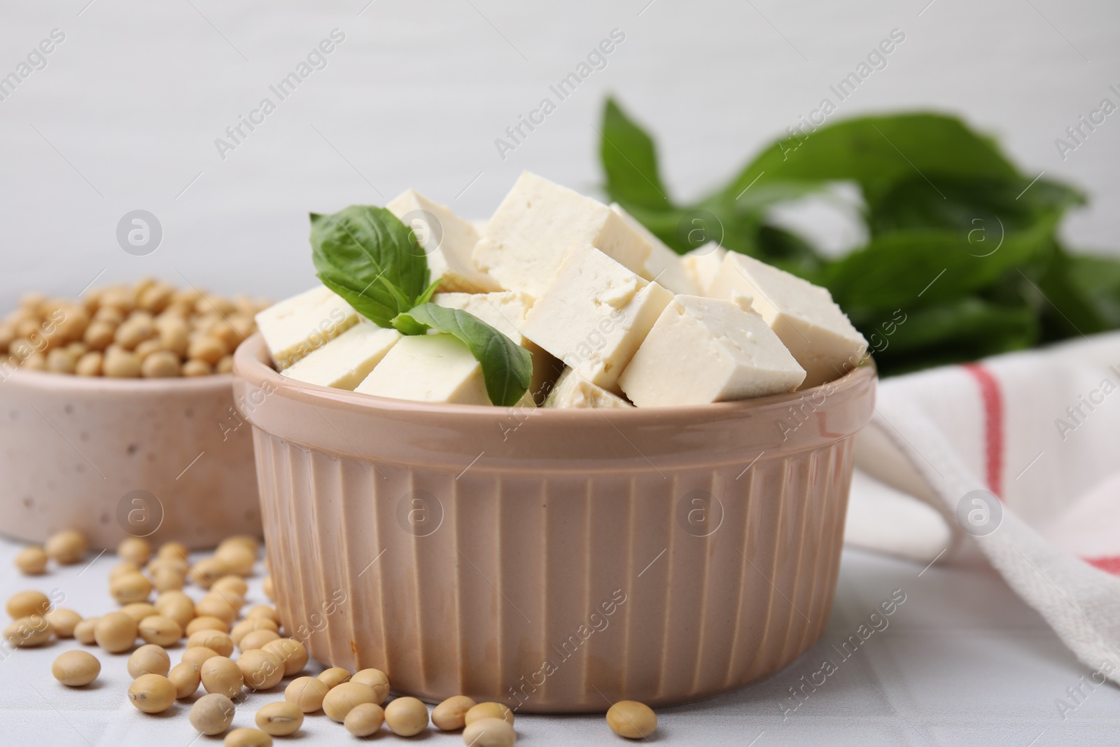 Photo of Delicious tofu cheese, basil and soybeans on white tiled table, closeup