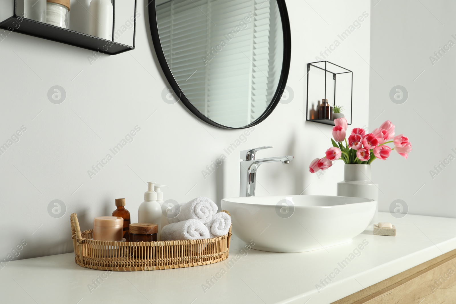 Photo of Vase with beautiful pink tulips and toiletries near sink in bathroom