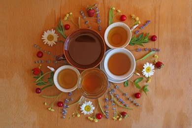 Photo of Cups with tasty herbal tea, different flowers and fruits on wooden table, flat lay