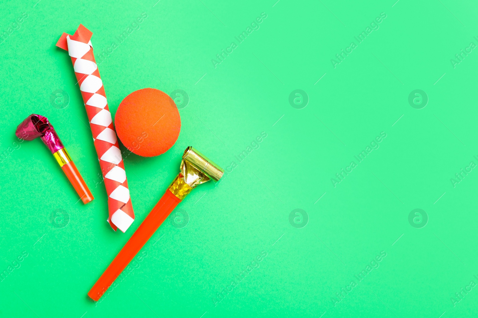 Photo of Party blowers, clown nose and chinese finger trap on green background, flat lay. Space for text