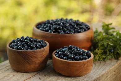 Photo of Bowls of delicious bilberries on wooden table outdoors, closeup
