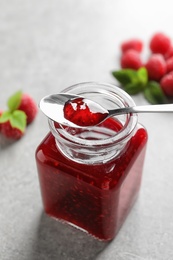 Glass jar and spoon of sweet raspberry jam on table