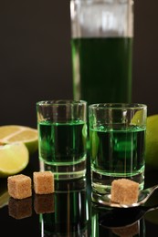 Absinthe in shot glasses, brown sugar, lime and spoon on mirror table. Alcoholic drink