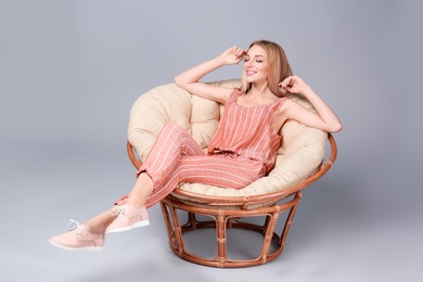 Photo of Young stylish woman with trendy shoes sitting in papasan chair on grey background