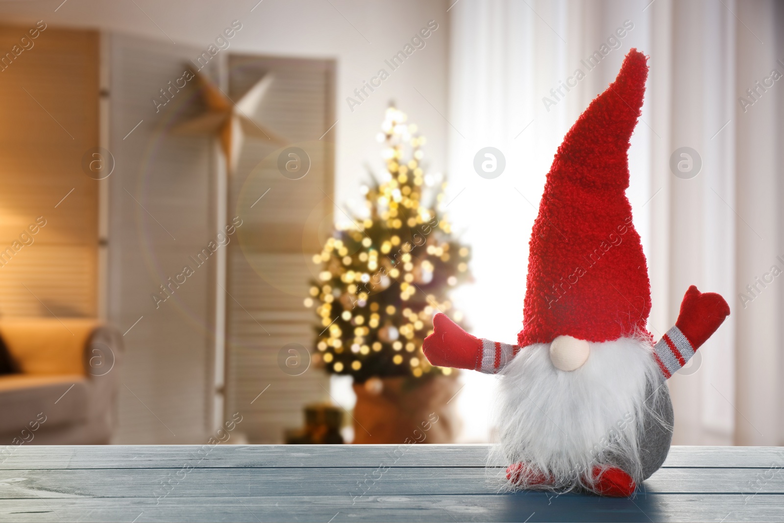 Image of Funny Christmas gnome on blue wooden table in room with festive decorations. Space for text