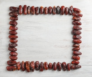 Photo of Frame made of sweet dried date fruits on wooden background, top view with space for text