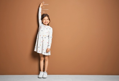 Photo of Little girl measuring her height near color wall