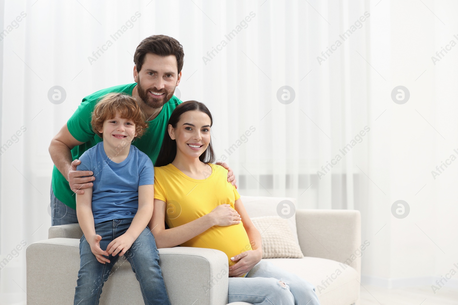 Photo of Family portrait of pregnant mother, father and son in house. Space for text