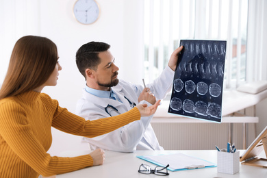 Orthopedist showing X-ray picture to patient at table in clinic