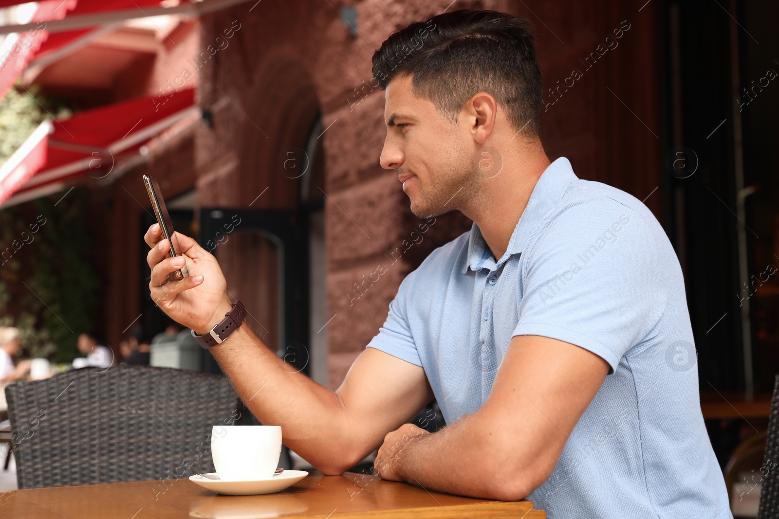 Photo of Man unlocking smartphone with facial scanner in outdoor cafe. Biometric verification