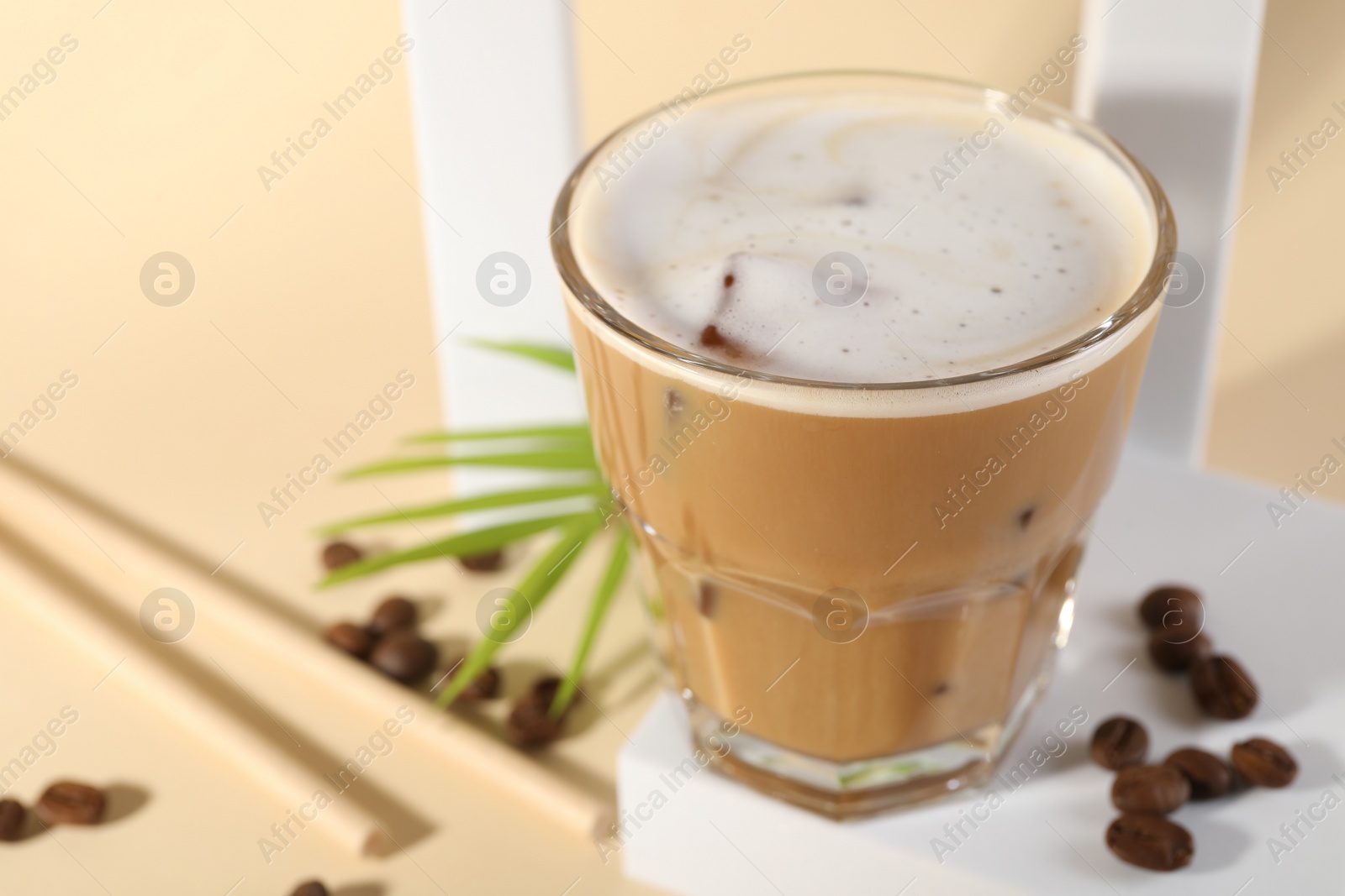 Photo of Refreshing iced coffee with milk in glass and beans on pale yellow background, closeup. Space for text