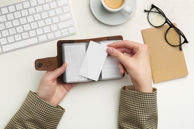 Photo of Woman holding leather business card holder with blank cards at white table, top view