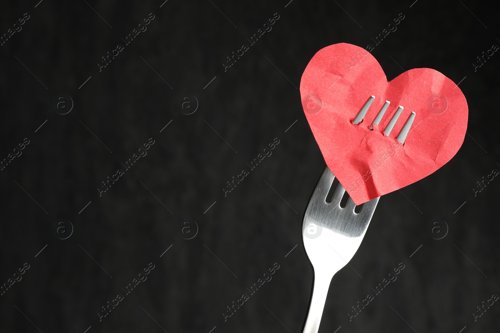 Photo of Broken heart. Red paper heart pierced with fork against black background, closeup. Space for text