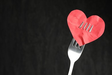 Photo of Broken heart. Red paper heart pierced with fork against black background, closeup. Space for text