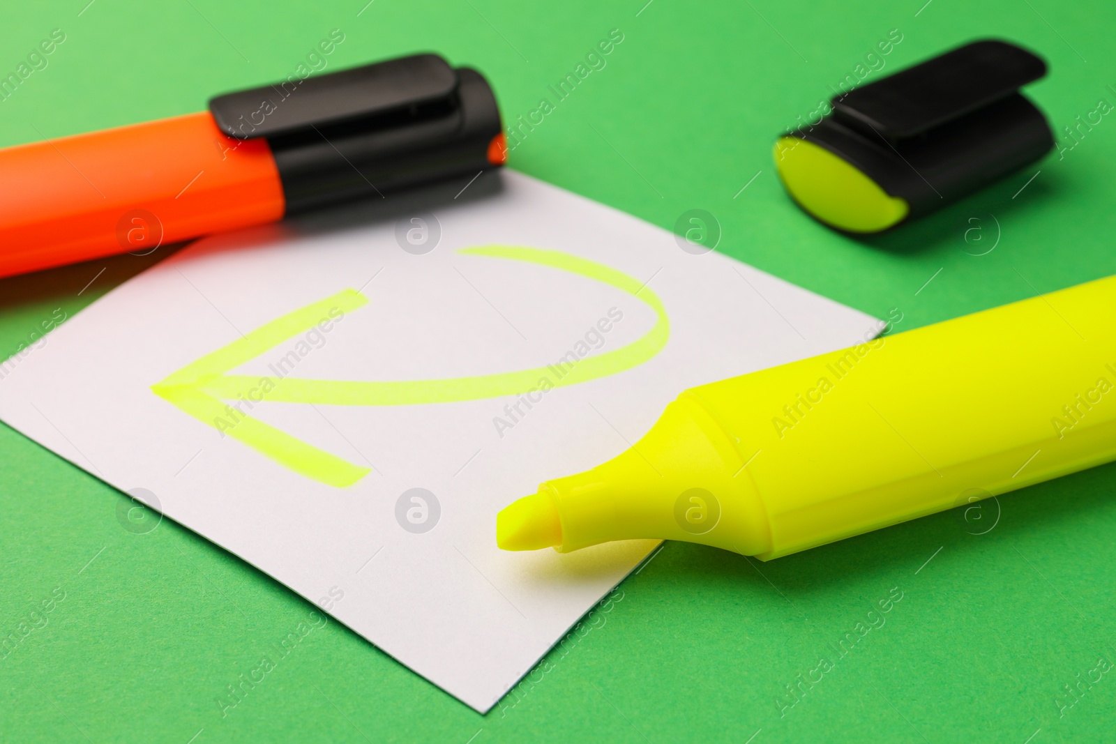 Photo of Bright color markers and sticky note with drawn arrow on green background, closeup
