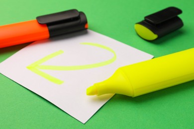Photo of Bright color markers and sticky note with drawn arrow on green background, closeup