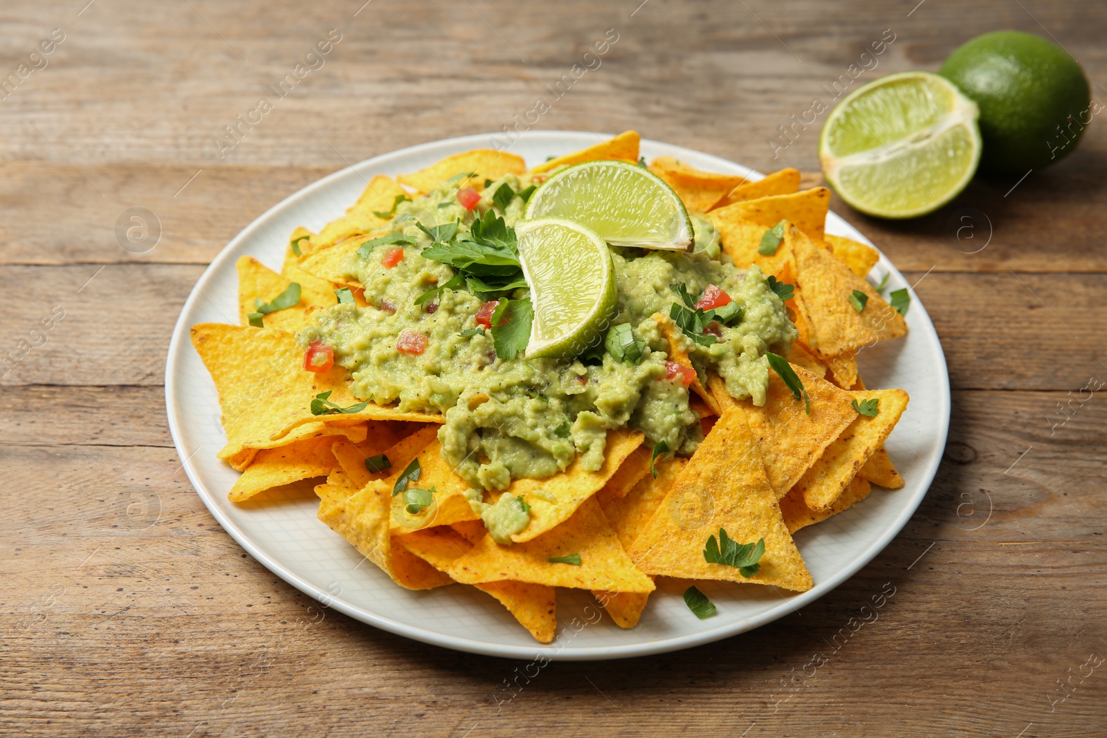 Photo of Plate of delicious mexican nachos chips with guacamole sauce and lime on wooden table