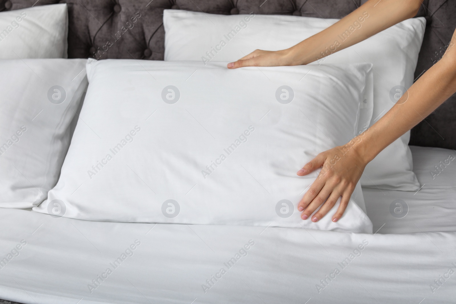 Photo of Young woman plumping white pillow on bed, closeup