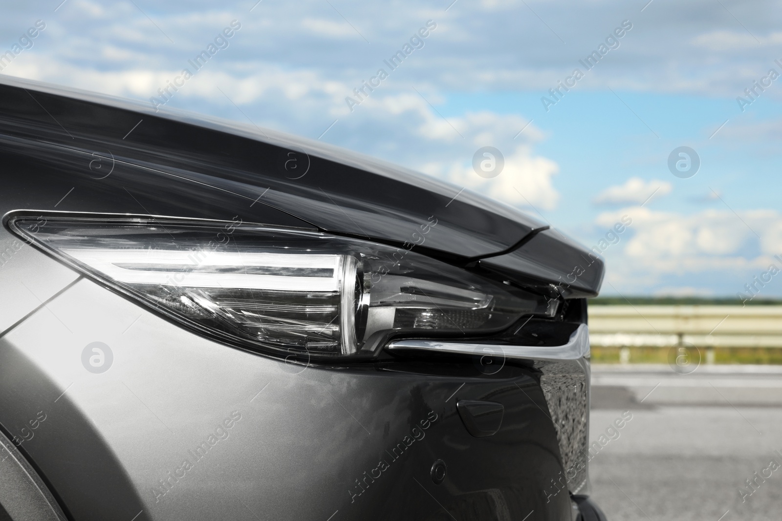 Photo of New black modern car against cloudy sky, closeup of headlight