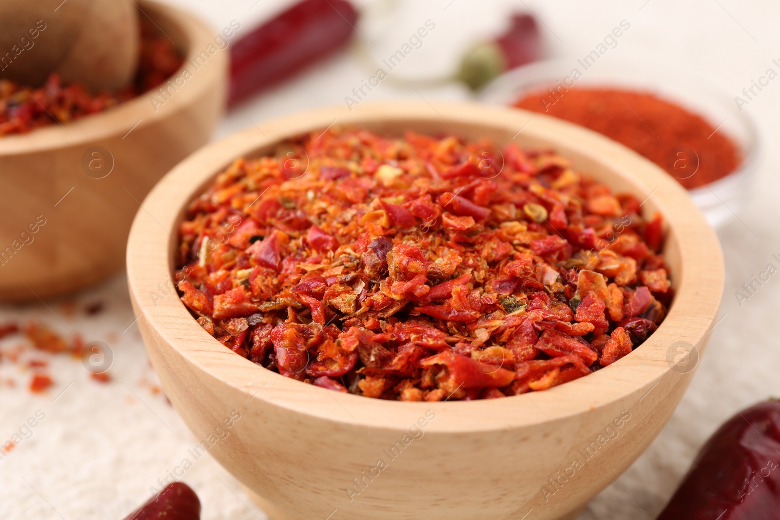 Photo of Chili pepper flakes and pods on light textured table, closeup