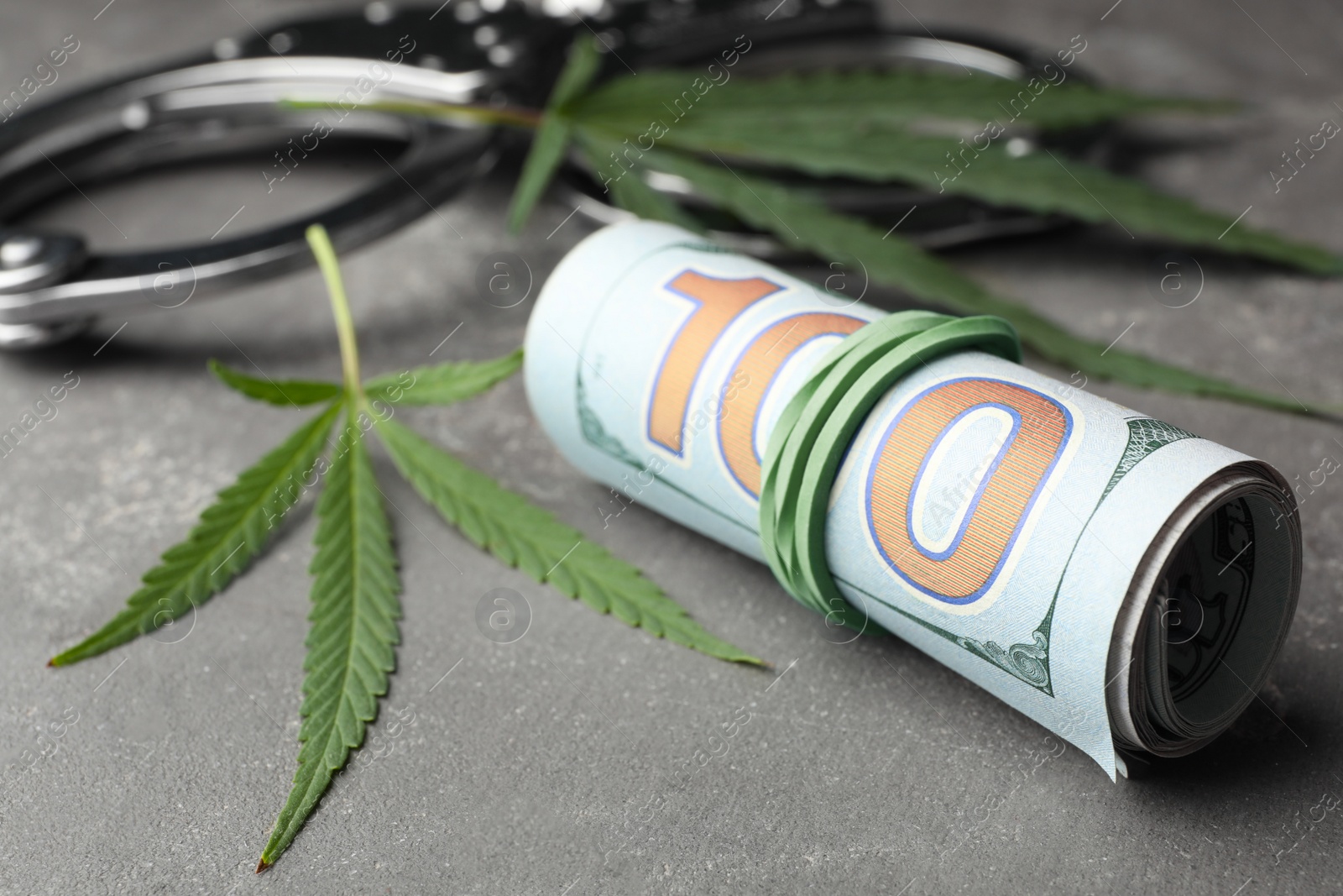 Photo of Hemp leaves, handcuffs and rolled money on stone grey background, closeup