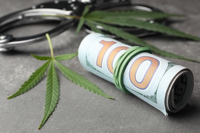 Photo of Hemp leaves, handcuffs and rolled money on stone grey background, closeup